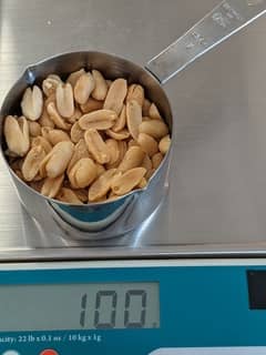 Scale with almost a full cup of peanuts weighing 100 grams