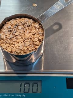 Scale with a cup of uncooked rolled oats weighing 100 grams